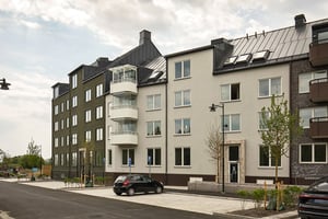 Flerbostadshus med balkonger och parkerade bilar på gatan