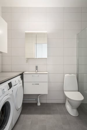 Modernt badrum med tvättmaskin, torktumlare, kommod med spegelskåp och toalett
