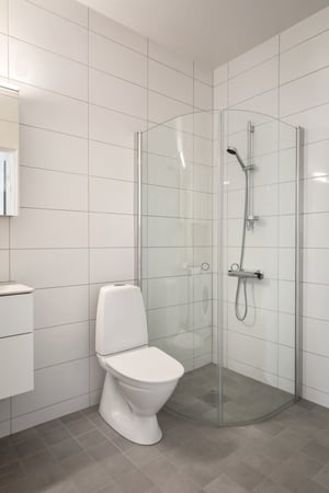 Badrum med toalett, duschhörna och vita kakelväggar