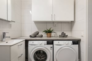 Tvättstuga med tvättmaskin och torktumlare under en bänkskiva, vitt kaklade väggar och handfat