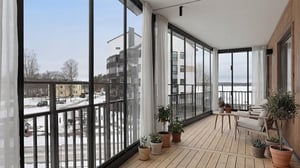 Inglasad balkong med ljusa sittmöbler, växter och utsikt över snötäckt område