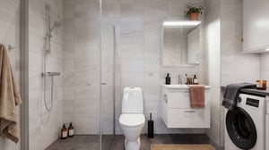 Badrum med dusch, toalett, handfat och tvättmaskin i ljusa kaklade ytor