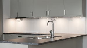 Modernt kök med gråa skåp, ljus stänkskyddsvägg, diskho och köksblandare