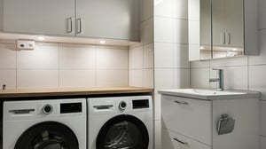 Badrum med två frontmatade tvättmaskiner, arbetsbänk och handfat med spegelskåp