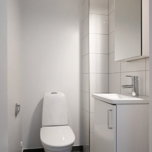 Litet, helkaklat badrum med toalett, handfat och spegelskåp i vitt