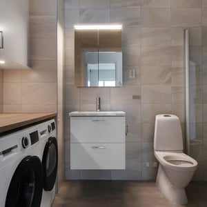 Tomt rum med kaklat badrum, tvättmaskin, kommod med spegelskåp och toalett