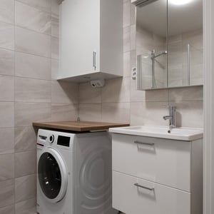 Praktisk tvättstuga med tvättmaskin, förvaringsskåp, handfat och spegelskåp i ljus kakelsättning