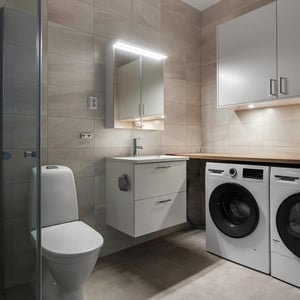 Modernt badrum med toalett, tvättställ med spegelskåp och tvättmaskiner under bänkskiva