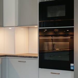 Inflyttningsklar lägenhet med modern köksinredning, ljusa skåp och inbyggd svart ugn samt mikrovågsugn