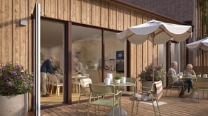 Personer sitter och umgås på en uteplats vid en modern träfasad med stora glaspartier