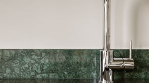 Köksbänk med vit vägg och grönt marmormönstrat stänkskydd samt en kromad köksblandare