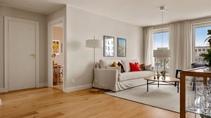 Lägenhet med ljus vardagsrumsdel, soffa, soffbord och stora fönster