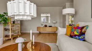 Vardagsrum med ljus inredning, beige soffa med färgglada kuddar, träbord och stora taklampor