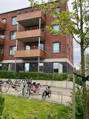 Flerfamiljshus med tegel- och putsfasad, balkonger och cykelställ framför byggnaden