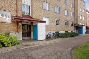 Flerbostadshus med fasad av gulbrun tegel, entré med blå dörrar och cyklar parkerade vid sidan