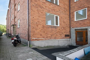 Flerfamiljshus med fasad i tegel, en gångväg, en parkerad moped och en entrédörr