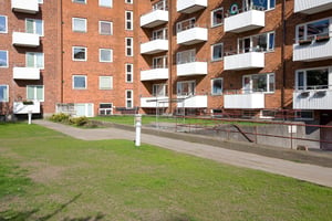 Flerfamiljshus i rött tegel med vita balkonger och en gräsmatta framför
