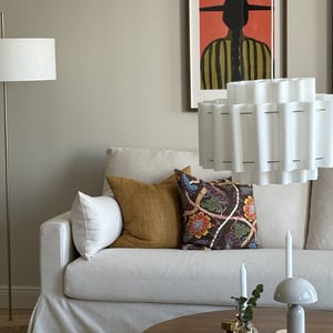 Vardagsrum med ljus soffa, dekorativa kuddar, golvlampa och väggkonst