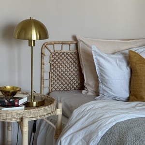 Sänghörna med vit och beige bäddning samt sängbord med gul lampa