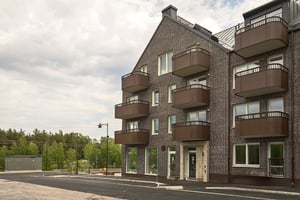 Flerfamiljshus i tegel med balkonger och entré, omgivet av grönska