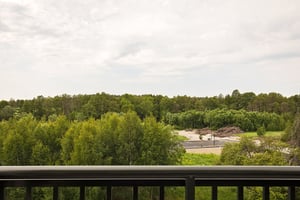 Utsikt från balkong över grön skog och en byggarbetsplats i fjärran