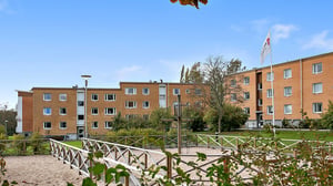 Flerfamiljshus i tegel med sandlåda och grön innergård under klarblå himmel