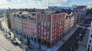 Flerfärgat bostadskvarter med moderna fasader, omgivande träd och en bred gata under en klar himmel