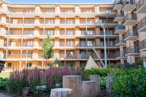 Flerfamiljshus med balkonger och grön innergård med blommor och träpallar
