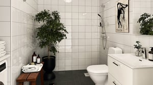 Badrum med vita kakelväggar, mörkt golv, dusch, toalett, handfat och grön växt