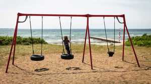 Barn som gungar på en bildäcksgunga vid stranden, med havet i bakgrunden