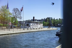 Båtbrygga vid vatten med en vit ångbåt och flaggor i solsken