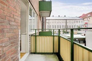 Balkong med gröna räcken och gul panel, anslutande till en tegelbyggnad, med utsikt mot en innergård och omgivande byggnader