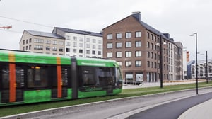 Grön spårvagn passerar framför moderna flerfamiljshus i stadsmiljö