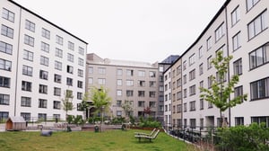 Flerfamiljshus med ljusa fasader runt en innergård med gräs, sittplatser och träd