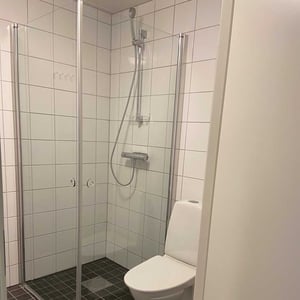 Inflyttningsklart badrum med duschhörna, vita kakelväggar och toalett