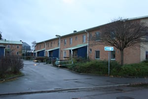 Radhusområde med tegelbyggnader, parkeringsplats och växtlighet under en mulen himmel. En pilskylt syns vid infarten