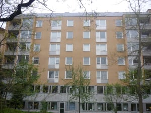 Gul flerfamiljsbyggnad med sex våningar, omgiven av träd och buskar