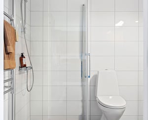 Inflyttningsklart badrum med dusch, vita kaklade väggar och toalett