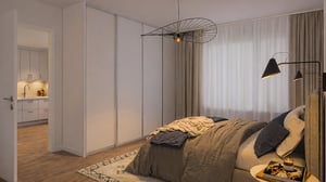 Sovrum med en dubbelsäng, beige gardiner, taklampa och golvlampa. En dörr leder till ett kök med ljusa skåp och träfärgat golv