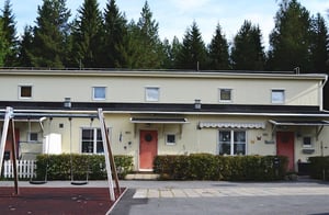 Radhuslänga med beige fasad, röda entrédörrar och träd framför