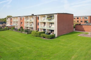 Flerfamiljshus med röda tegelväggar och balkonger, omgivna av en grön gräsmatta under en klar blå himmel