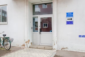 Vit entrédörr med glaspartier på en byggnad, cykel med korg parkerad till vänster, och skyltar som indikerar parkeringsregler på väggen