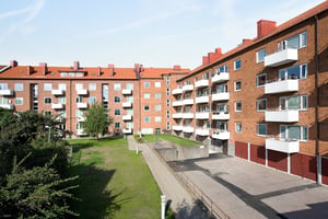 Flerfamiljshus i rött tegel med balkonger och en grön innergård under en klar himmel