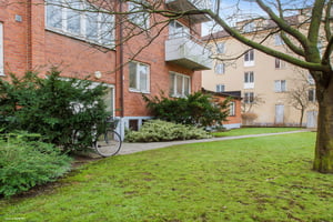 Flerbostadshus i tegel med grönskande trädgård, gräsmatta och en cykel vid sidan