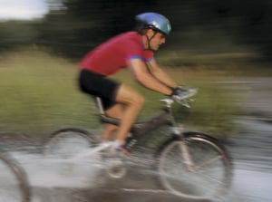 Person cyklar på en stig genom vatten, med hjälm och röd cykeltröja