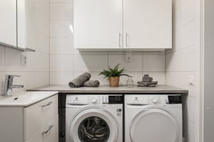 Tvättstuga med tvättmaskin och torktumlare under en bänkskiva, vitt kaklade väggar och handfat