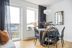 Ljust matrum med stora fönster, svart matbord med svarta stolar, randig bordsduk och dekorativ spegel på väggen