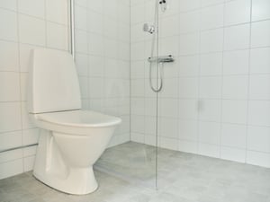 Badrum med toalett, duschhörna och vita kakelväggar