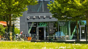 Bageri och café med uteservering i stadsmiljö, omgivet av gröna träd och cyklar