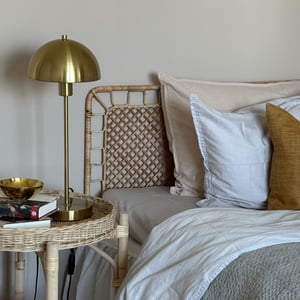 Sänghörna med vit och beige bäddning samt sängbord med gul lampa